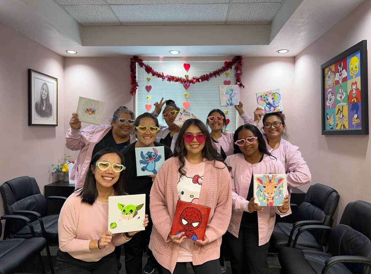 The orthodontic team smiling, wearing heart glasses, and holding up paintings